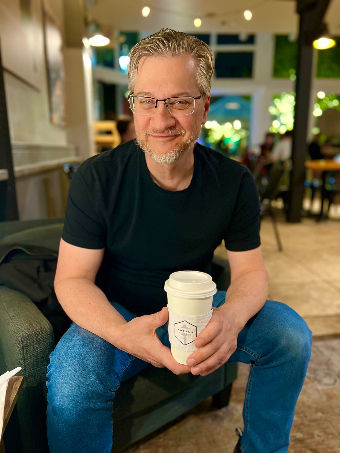 Tim Ristow smiling in a warm café, holding a coffee cup